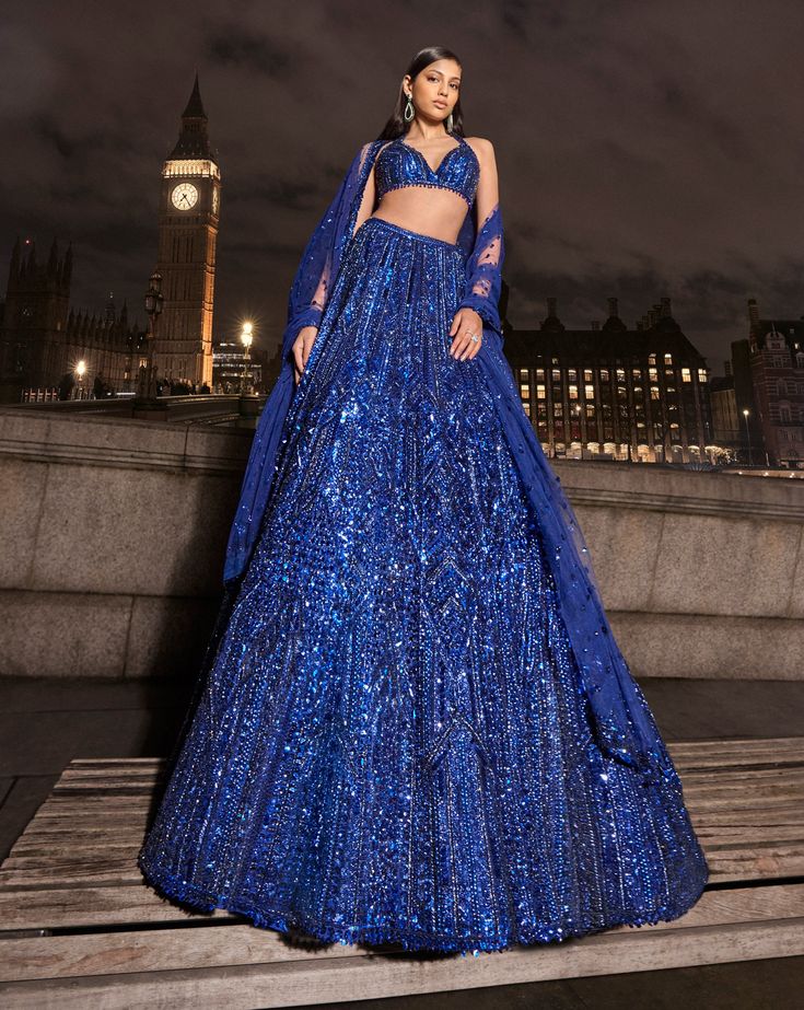 This navy lehenga set features all over tonal sequin embroidery in a geometric pattern. The ensemble is paired with a strappy blouse with tassels at the waist and a matching net dupatta.From Seema Gujral's For the love of London collection. DELIVERY TIMEPlease allow 8-12 weeks for your outfit to arrive. FABRIC DETAILSNet Professional cleaning only. Blue Sequined Sets For Reception, Glamorous Blue Lehenga With Zari Work, Dusty Blue Lehenga, Blue Glamorous Lehenga For Reception, Glamorous Blue Lehenga For Festive Occasions, Blue Sequined Party Wear Choli, Blue Evening Lehenga, Glamorous Blue Lehenga For Evening, Blue Sequined Lehenga For Diwali