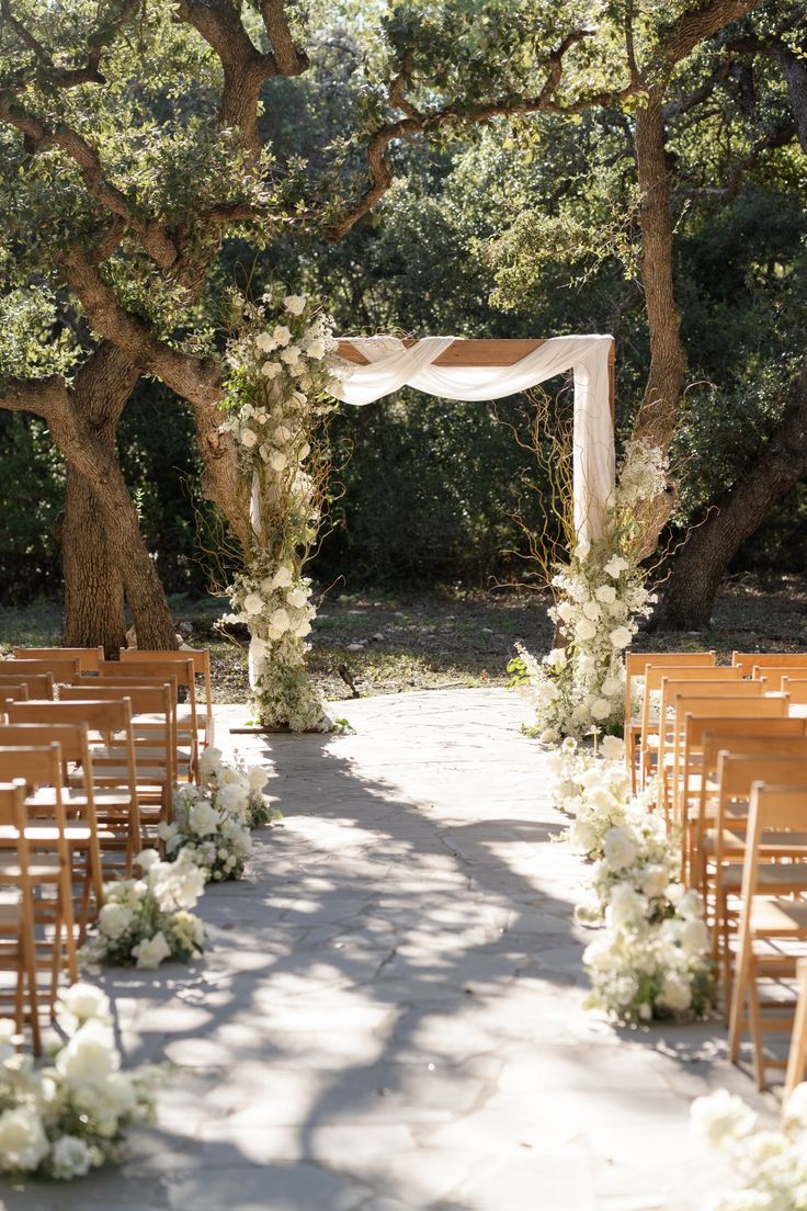 an outdoor ceremony setup with white flowers and greenery on the aisle, surrounded by trees