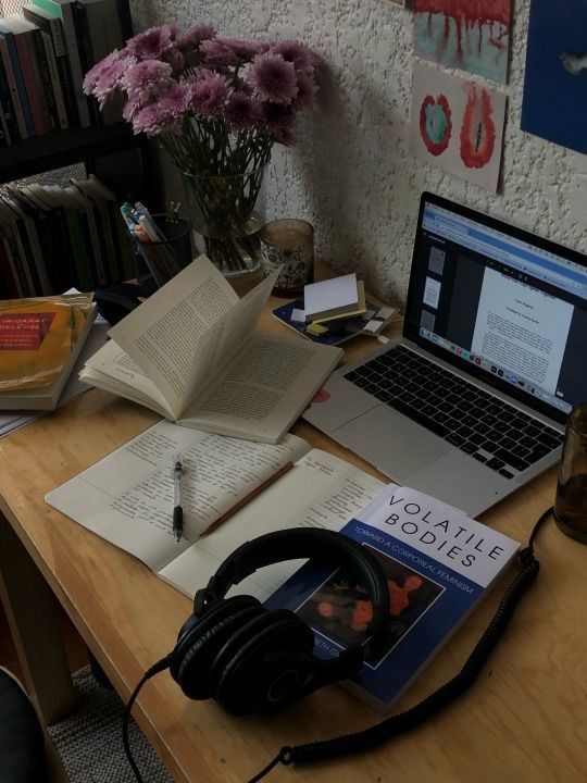 a laptop computer sitting on top of a wooden desk next to books and headphones