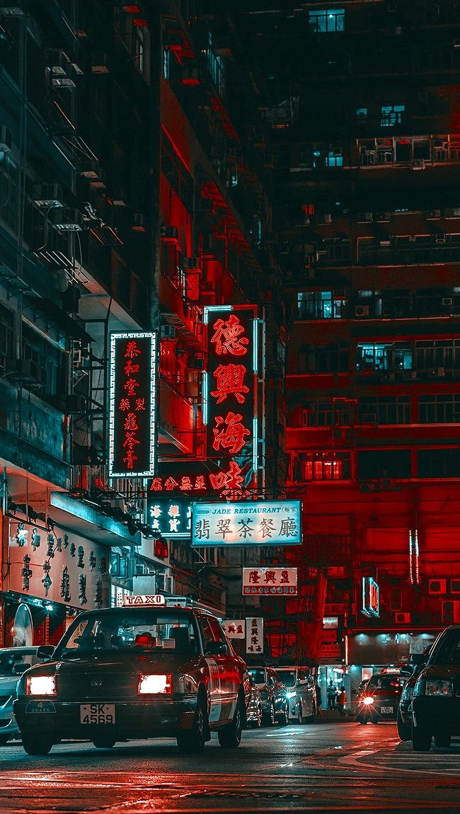 cars are parked on the street in front of tall buildings with neon lights at night