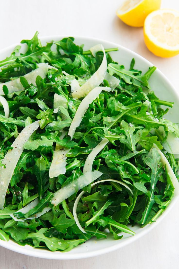 a white bowl filled with greens and sliced lemons