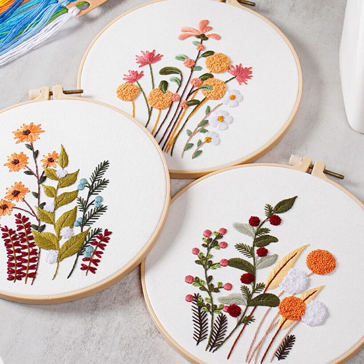 three embroidery hoops with flowers on them sitting on a table next to some scissors