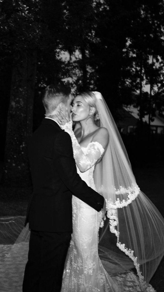 a bride and groom kissing in front of the trees at their wedding reception, black and white photo