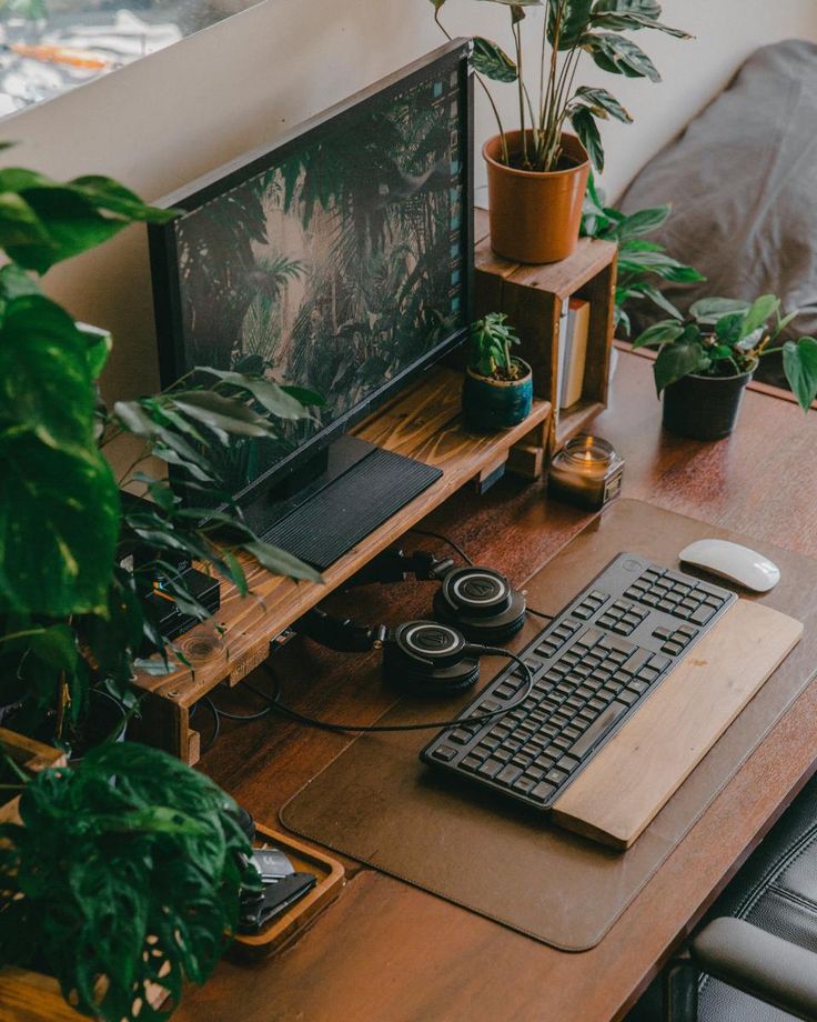 a desk with a keyboard, mouse and monitor on it next to some potted plants