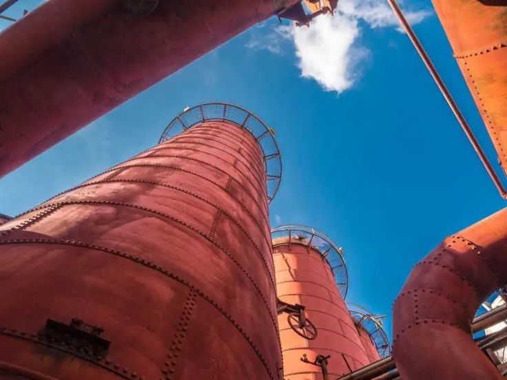 looking up at the top of two large industrial tanks with sky in the back ground