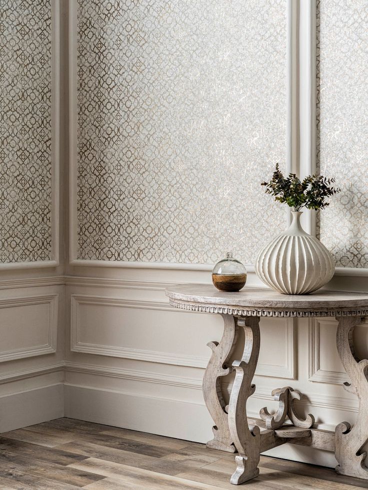 a table with a vase on top of it next to a wallpapered wall