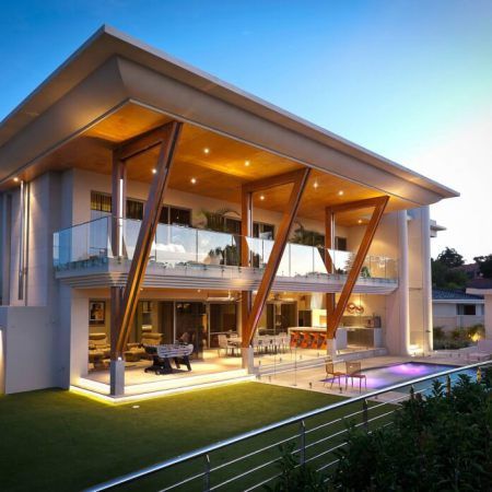 a large modern house with an outdoor deck and pool area at night time in the evening