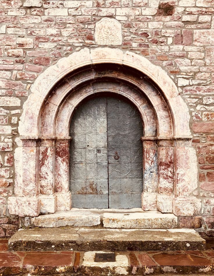 an old stone building with a wooden door and arched window in the center, surrounded by bricks