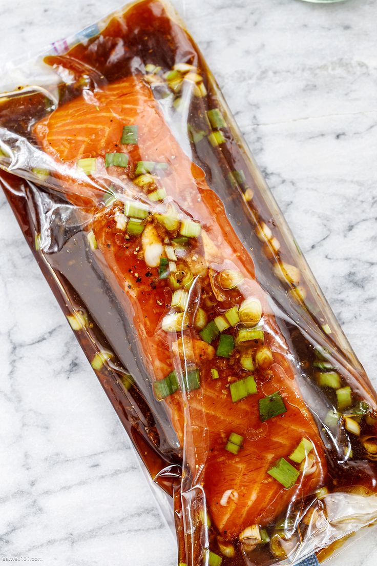 two pieces of salmon wrapped in plastic sitting on a marble counter top with green onions and seasoning