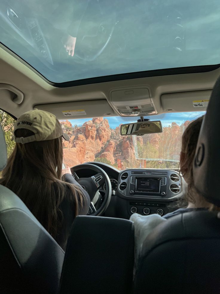 two people sitting in the passenger seat of a car looking out at mountains and trees