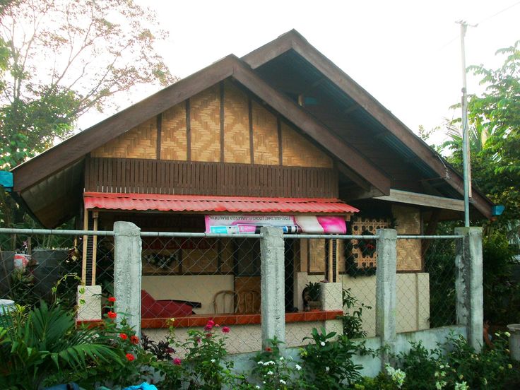 a small house with lots of plants and flowers around it's front porch, next to a chain link fence