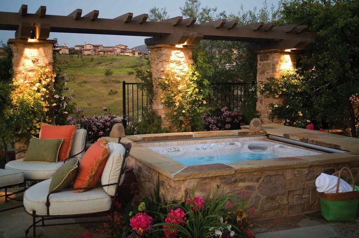 an outdoor hot tub surrounded by patio furniture and flowers in the foreground with lights above it