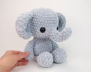 a hand holding a small blue crocheted elephant