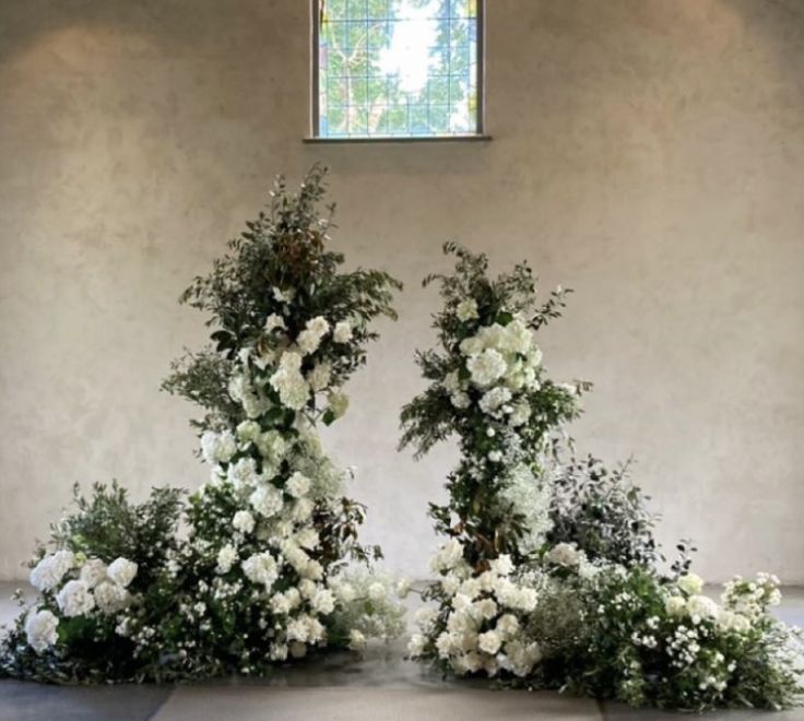 three white flowers are arranged on the floor in front of a window with a stained glass pane