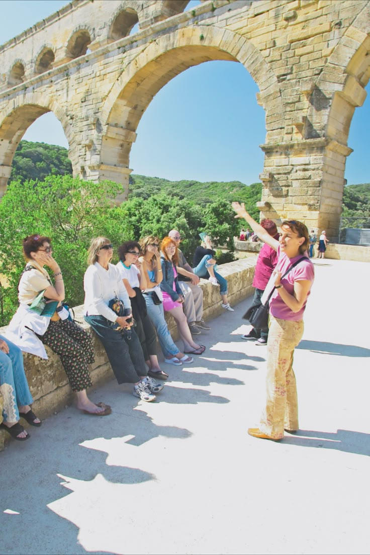 a group of people sitting and standing next to each other near an old stone wall