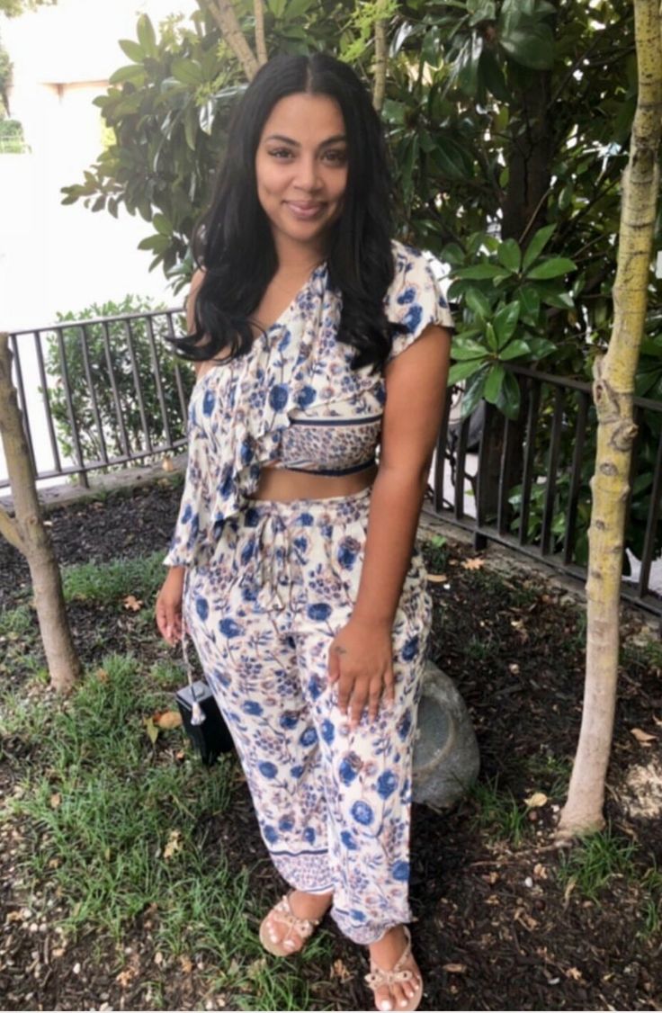 a woman standing in front of a tree wearing sandals and a blue floral print dress