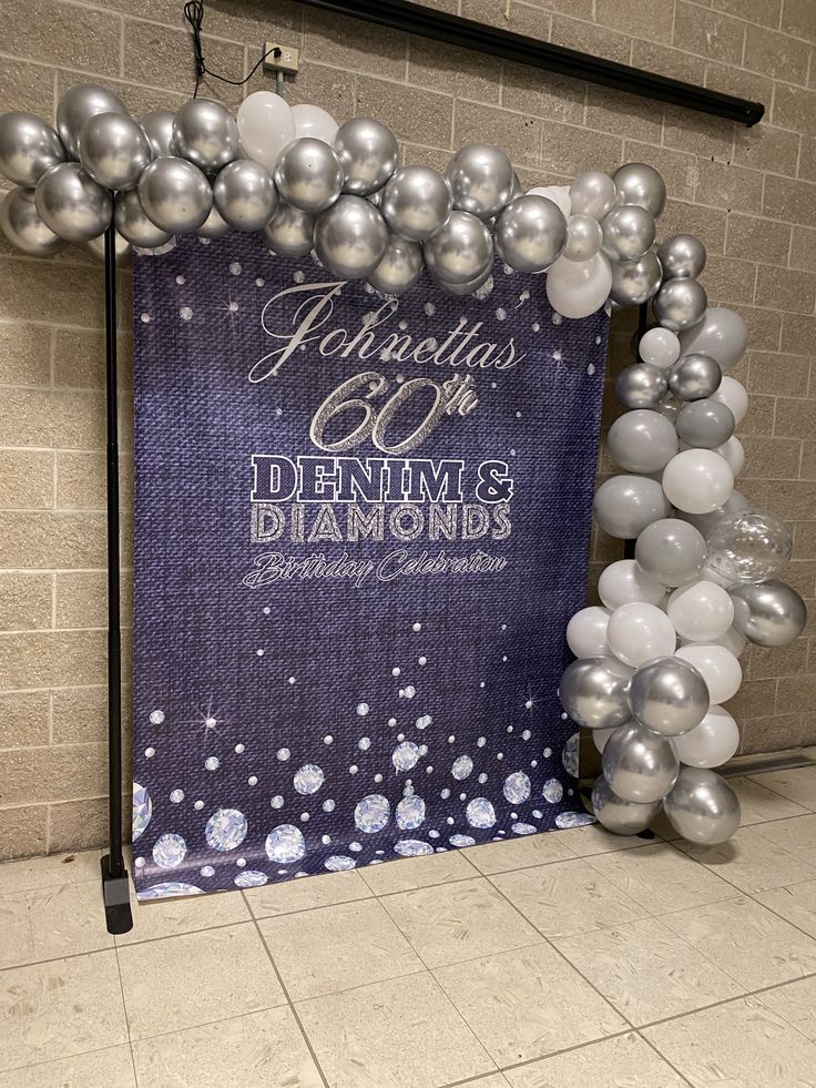 a large balloon arch with silver and white balloons in front of a sign that reads celebrating 60th denim's diamonds