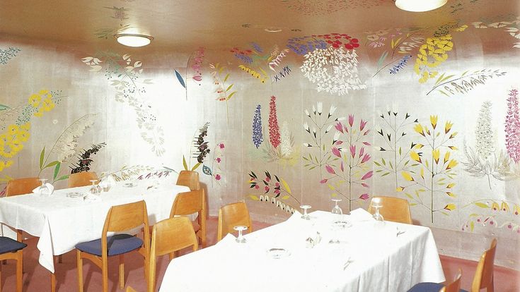 a dining room with white table cloths and colorful flowers on the wall