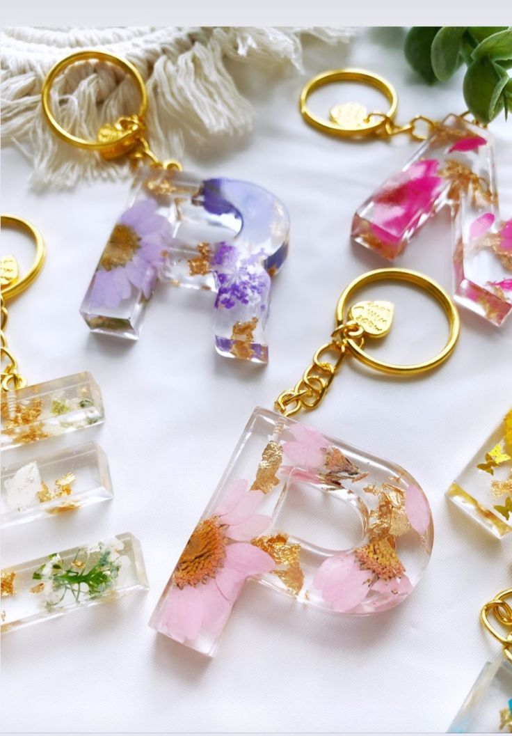 the letters are made out of glass and have flowers on them, as well as gold - plated key chains