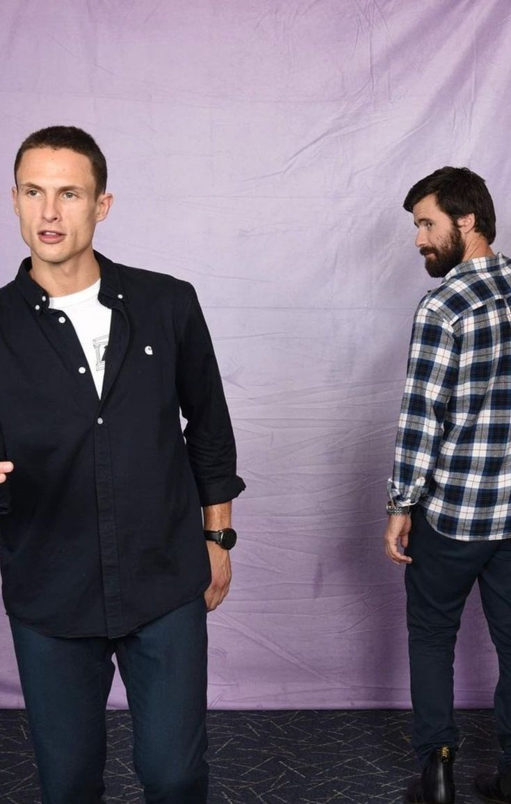 two men standing next to each other in front of a purple backdrop with one man pointing at the camera