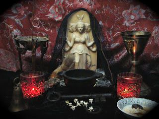 an assortment of decorative items displayed in front of a red wallpapered background, including a statue and candles