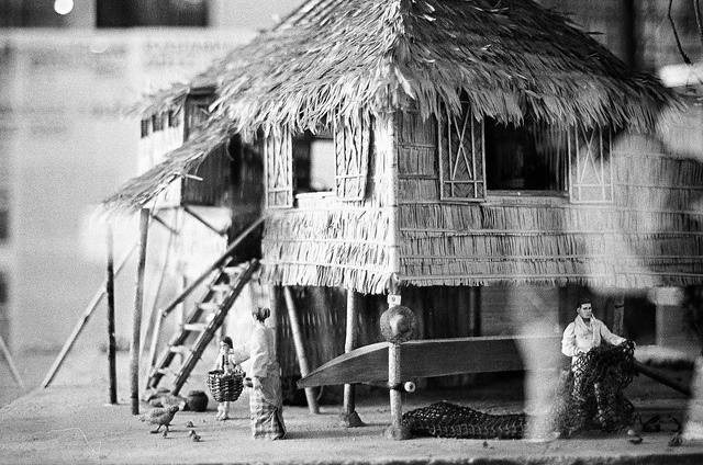 a black and white photo of a house made out of straw with people standing outside