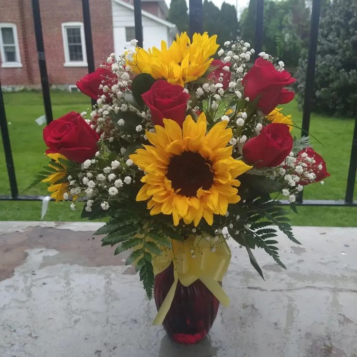 a vase filled with sunflowers and roses on top of a stone table next to a fence