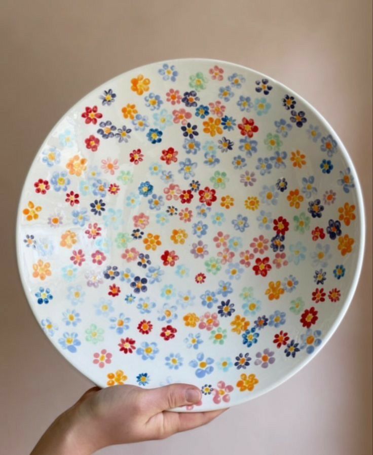 a hand holding a plate with colorful flowers on it