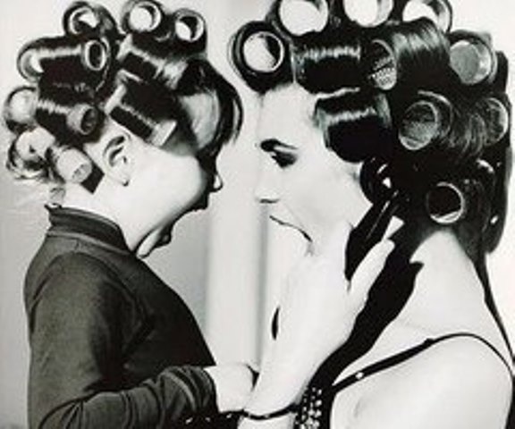 black and white photograph of two women with hair dryers on their heads looking at each other