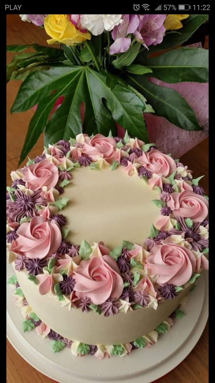 a white cake with pink and purple frosting on a table next to some flowers