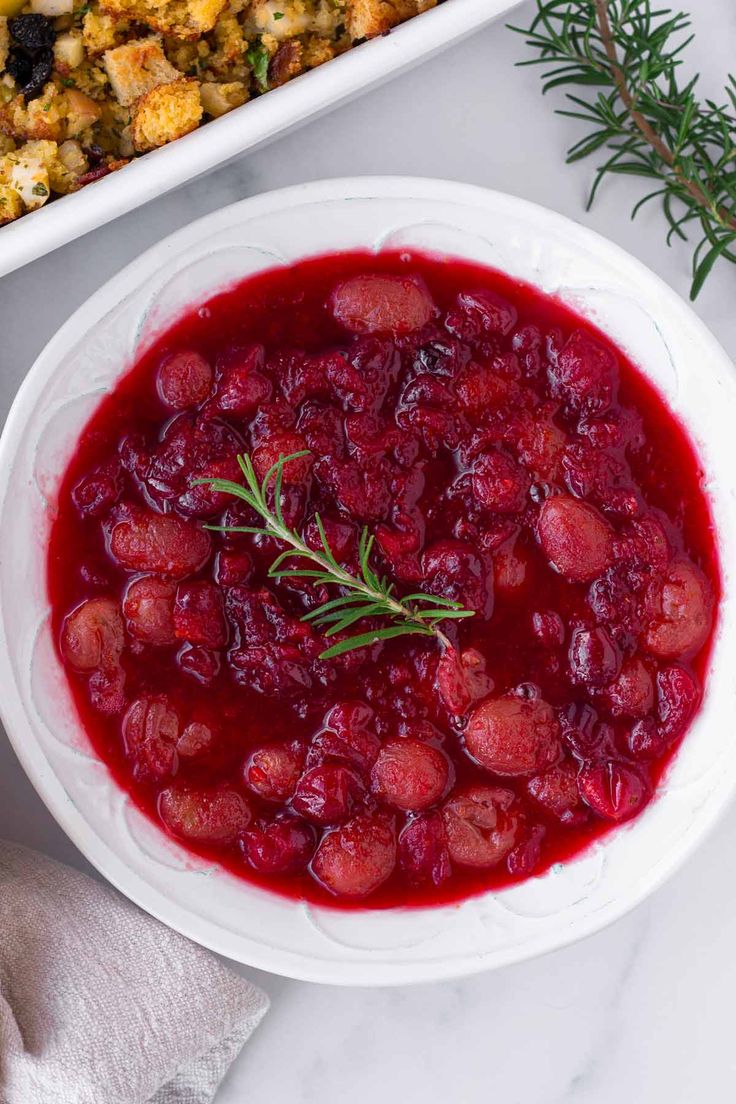 a white bowl filled with cranberry sauce next to a casserole dish