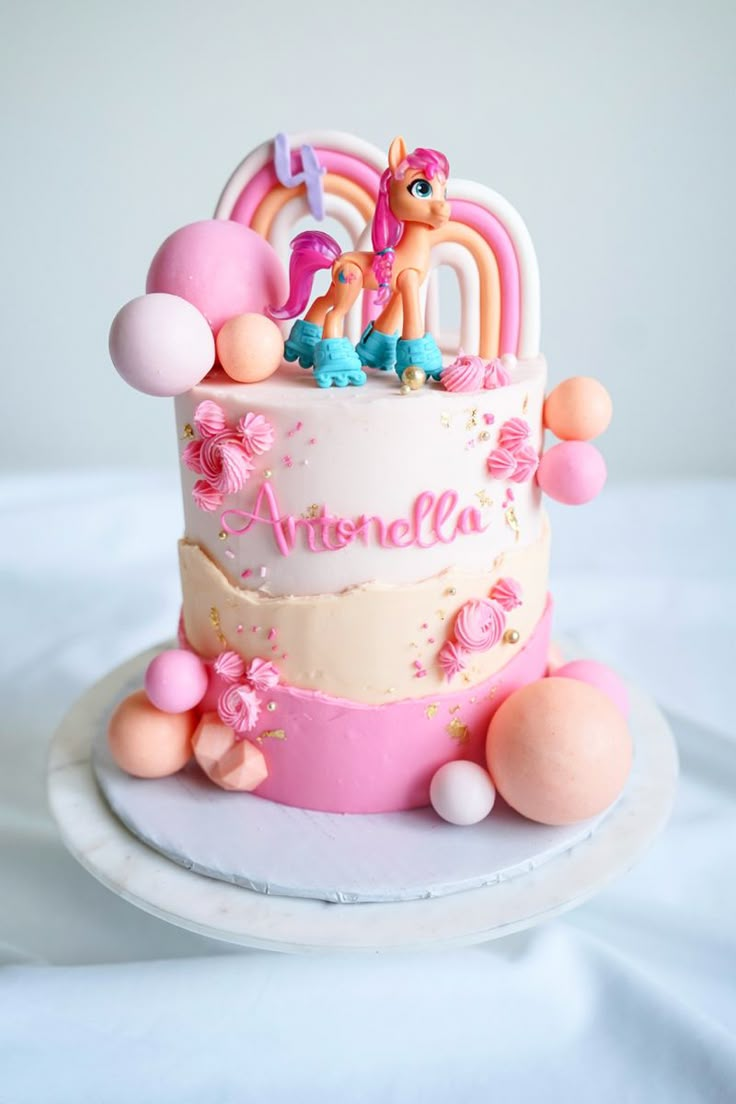 a pink and white birthday cake with pony on it's top, surrounded by balloons