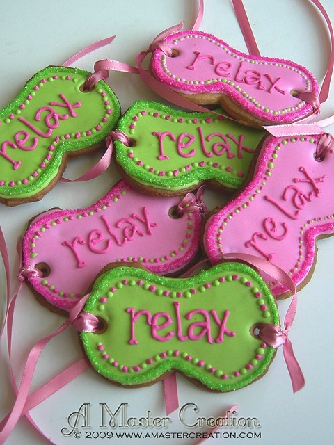 some pink and green decorated cookies on a white plate with ribbon around the edges that say relax