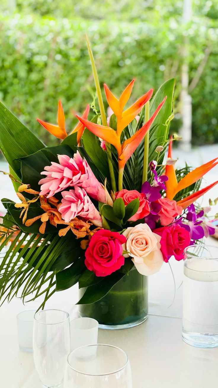 a vase filled with lots of colorful flowers on top of a table next to two glasses