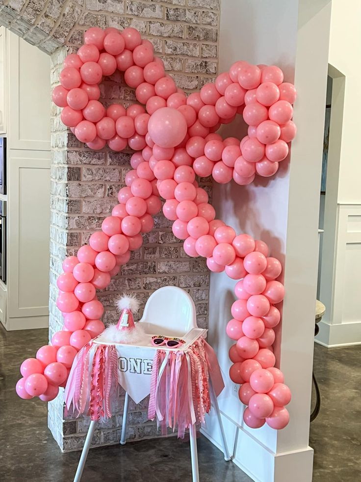 pink balloons are arranged in the shape of an x on a brick wall behind a white chair