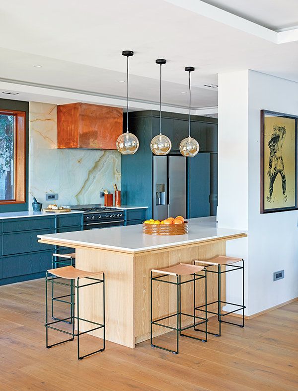 a kitchen with wooden floors and blue cabinets is pictured in this image, there are three stools at the center of the island