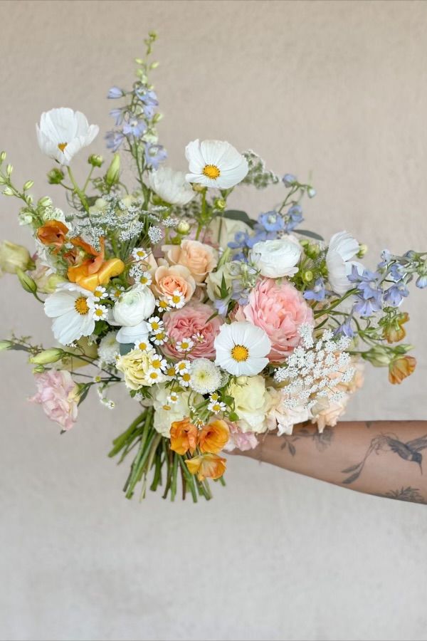 a woman holding a bouquet of flowers in her hand with tattoos on it's arm