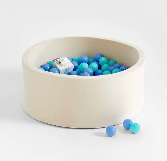 a white bowl filled with blue and green balls on top of a white table next to some candy