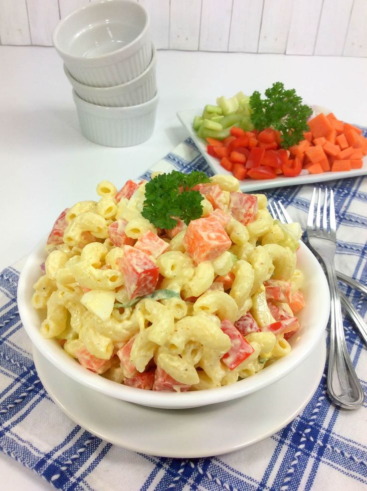 a white bowl filled with macaroni salad next to carrots and celery