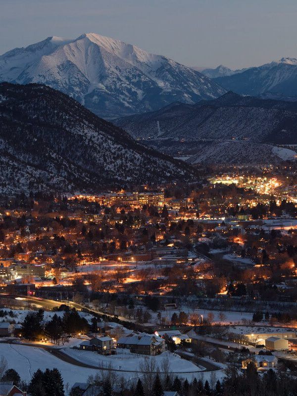 the city lights are lit up at night in the mountains