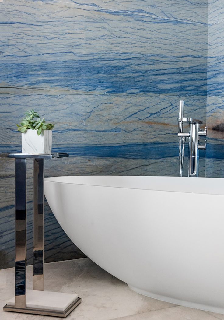 a white bath tub sitting next to a wall covered in blue and gray watercolors