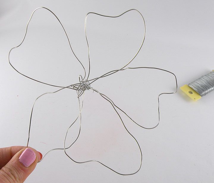 a hand holding a piece of wire with a flower design on it next to a thread spool