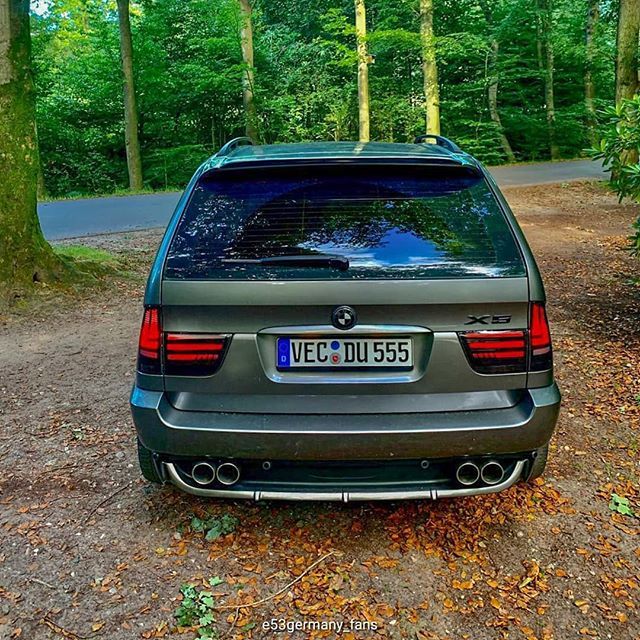 the back end of a car parked on a dirt road in front of some trees