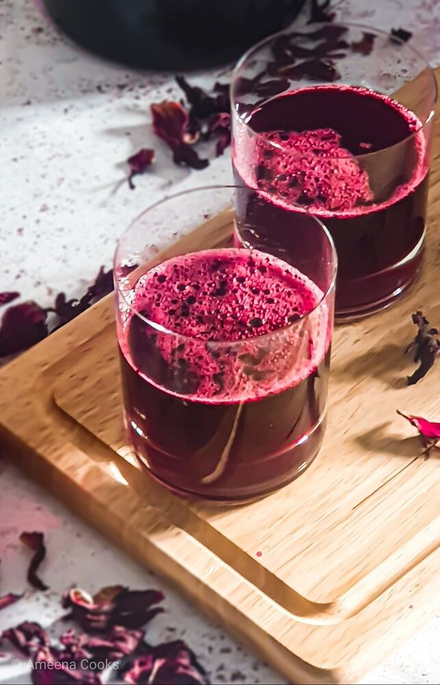 two glasses filled with red liquid sitting on top of a cutting board