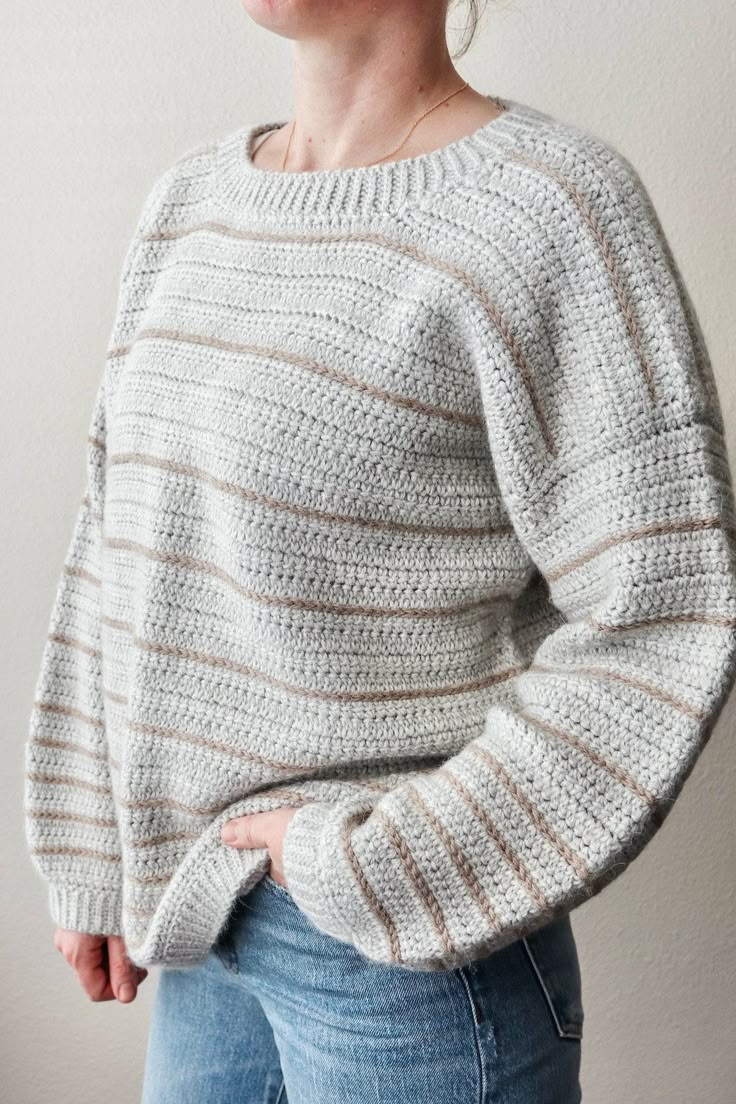 a woman wearing a white sweater and jeans standing in front of a wall with her hands on her hips