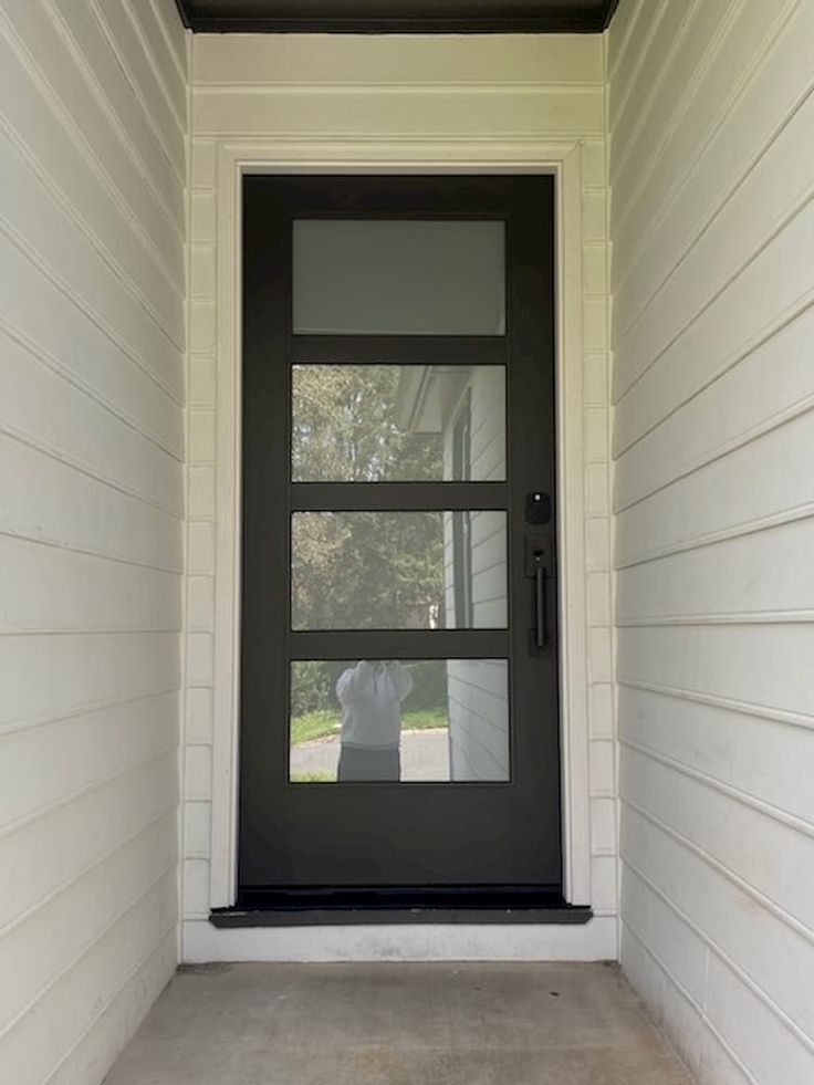 a black front door on the side of a white house with a dog in the window