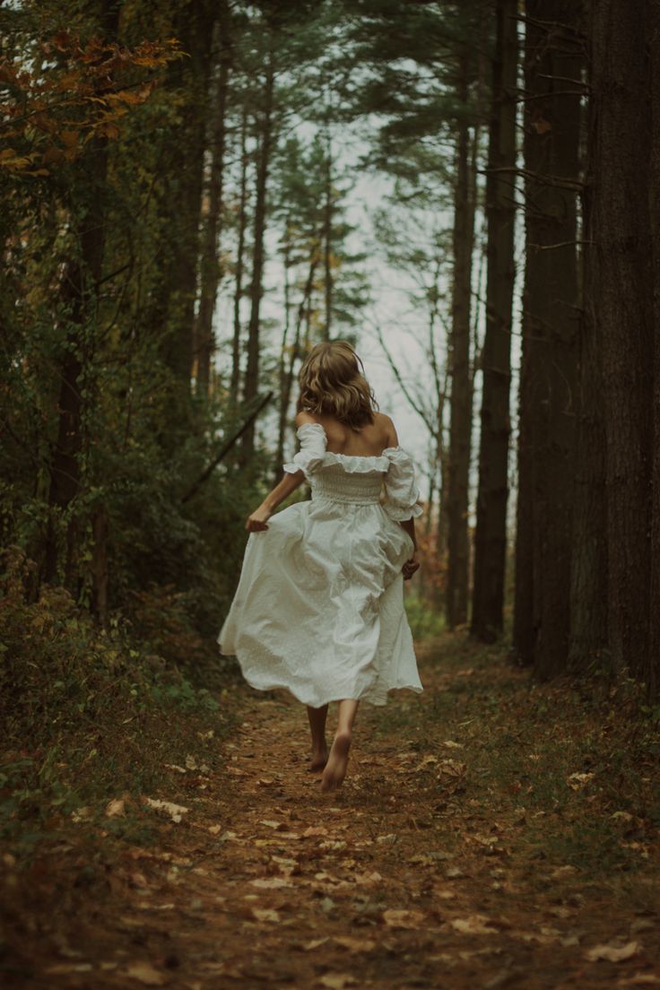 a woman in a white dress is walking through the woods