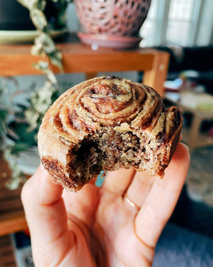 a hand holding a half eaten pastry in front of a table with potted plants