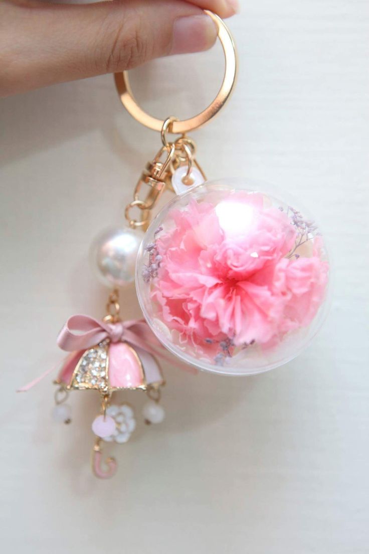 a hand holding a key chain with a pink flower in the center and a ball on it