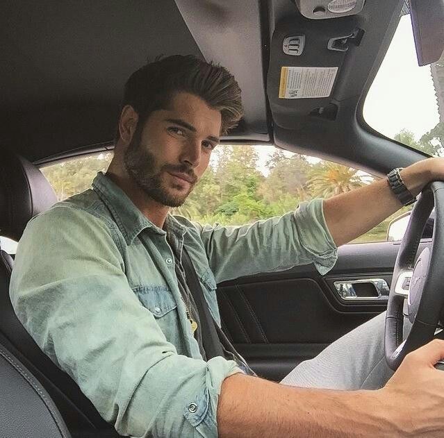 a man sitting in the driver's seat of a car with his hand on the steering wheel